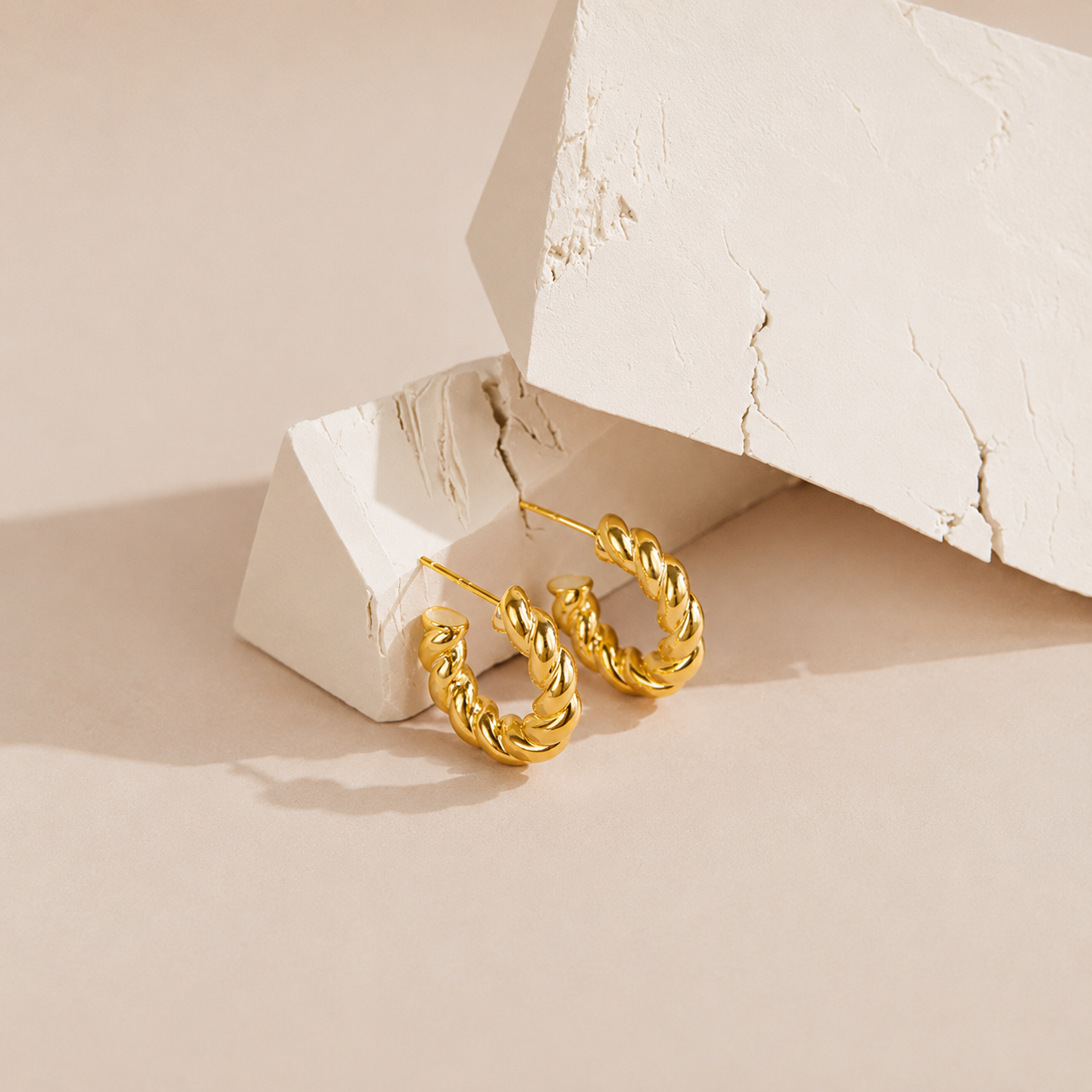 Gold hoop earrings on a textured beige surface
